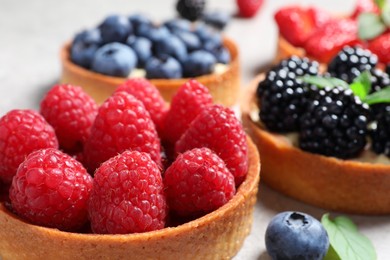 Photo of Tartlets with different fresh berries on light table, closeup. Delicious dessert