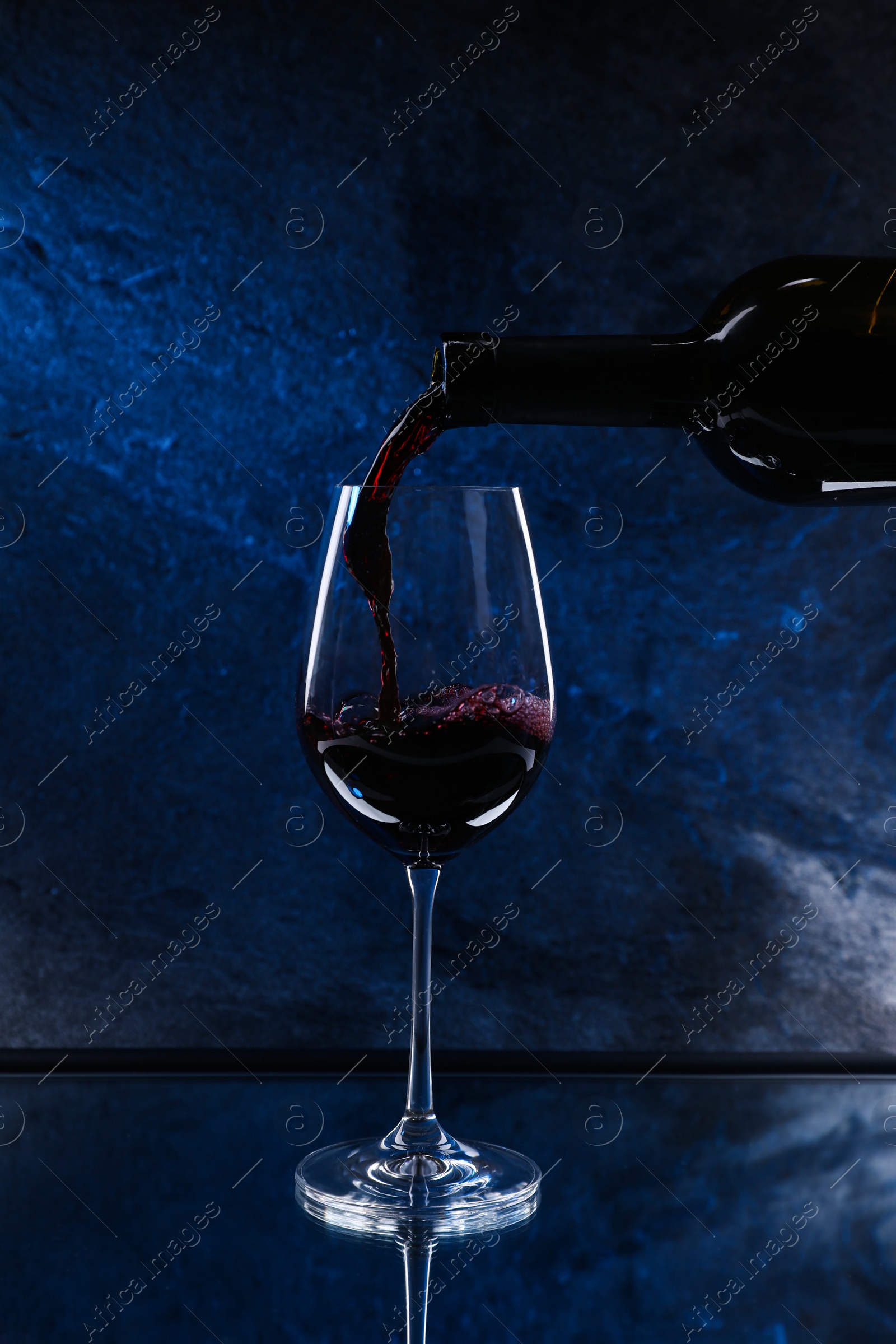 Photo of Pouring red wine from bottle into glass on color background