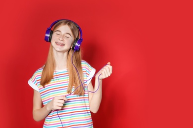 Teenage girl enjoying music in headphones on color background. Space for text