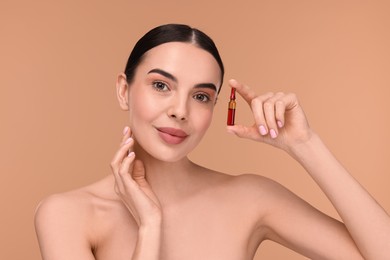 Photo of Beautiful young woman holding skincare ampoule on beige background