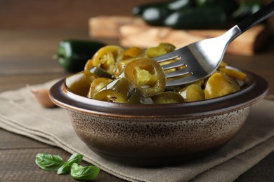 Photo of Taking slice of pickled green jalapeno with fork from bowl on wooden table