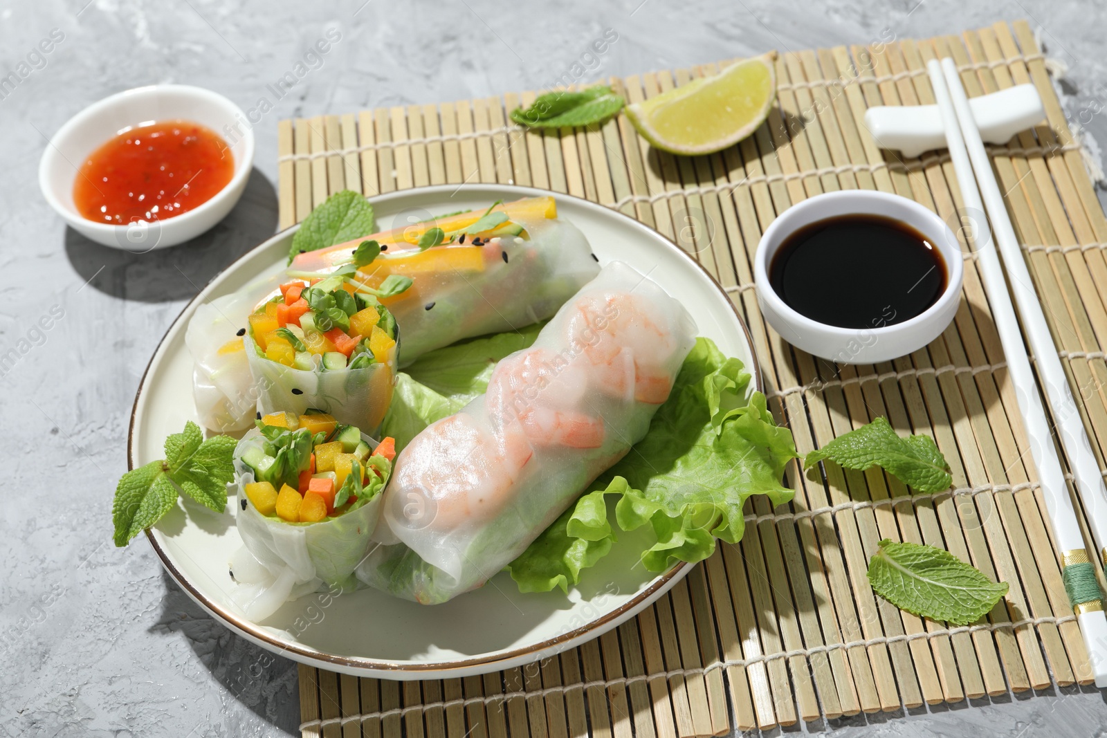 Photo of Tasty spring rolls and sauces on grey textured table, closeup