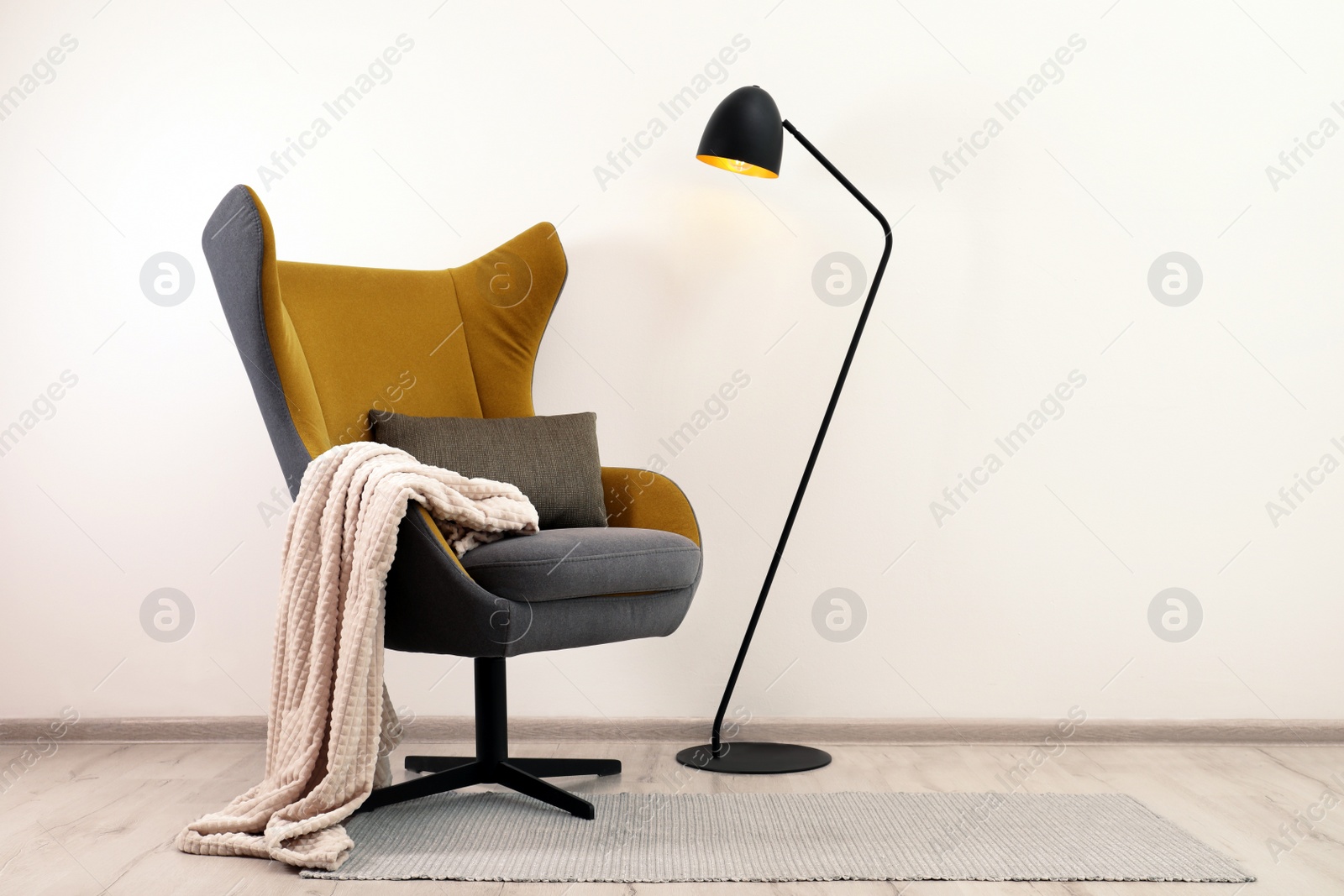 Photo of Comfortable armchair with blanket and floor lamp near white wall indoors