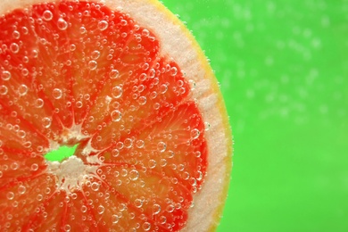 Photo of Slice of grapefruit in sparkling water on green background, closeup with space for text. Citrus soda