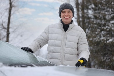Man cleaning snow from car hood outdoors