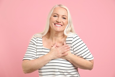 Photo of Mature woman holding hands near heart on color background