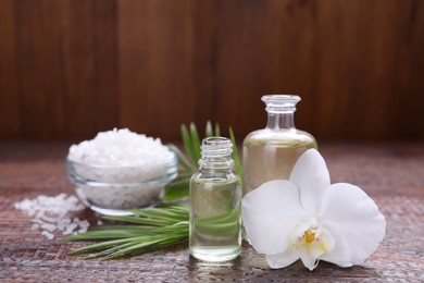 Photo of Essential oils, orchid flower and sea salt on wooden table, closeup