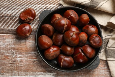 Fresh edible sweet chestnuts in frying pan on wooden table, flat lay
