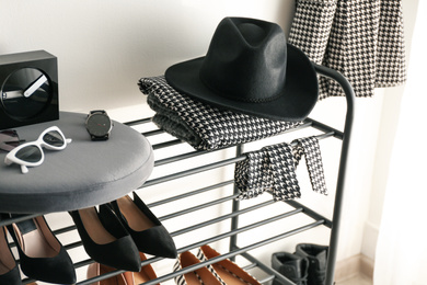 Photo of Black shelving unit with shoes and different accessories near white wall in hall