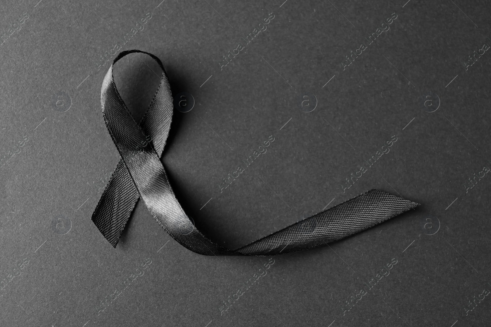 Photo of Black ribbon on dark background, top view with space for text. Funeral symbol