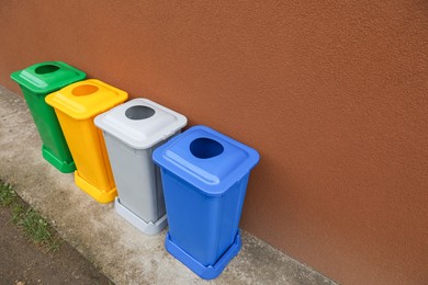 Many color recycling bins near brown wall outdoors, space for text