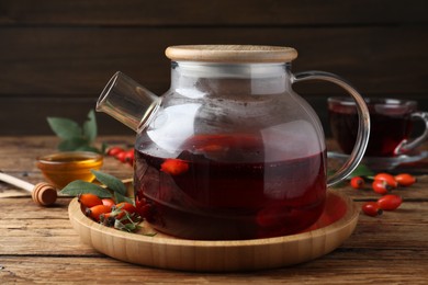 Photo of Teapot with aromatic rose hip tea and fresh berries on wooden table