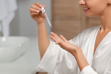 Woman applying cosmetic serum onto her hand in bathroom, closeup. Space for text