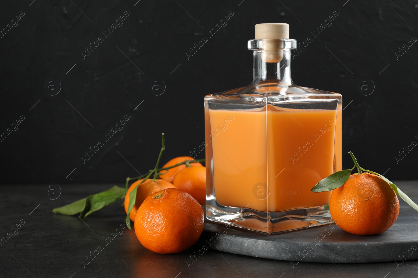 Photo of Delicious tangerine liqueur in glass bottle and fresh fruits on grey table, space for text