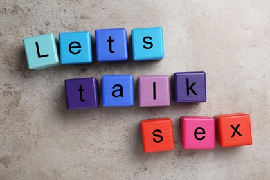 Photo of Colorful wooden blocks with phrase "LET'S TALK SEX" on stone background, flat lay