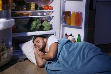 Photo of Young man sleeping near refrigerator at night