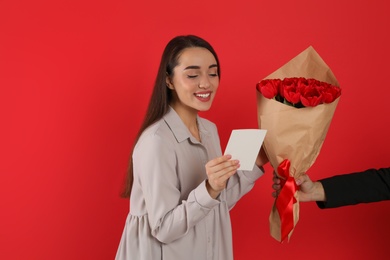 Photo of Happy woman receiving tulip bouquet from man on red background. 8th of March celebration