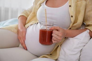 Photo of Pregnant woman with smoothie on bed, closeup. Healthy diet