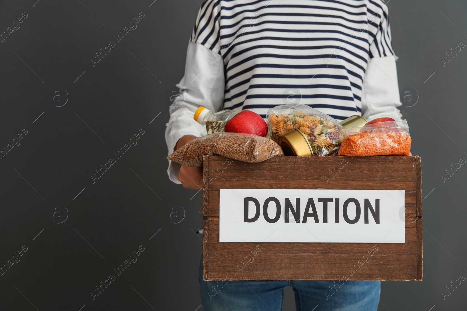 Photo of Woman holding donation box with food on gray background, closeup