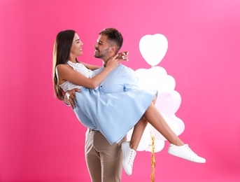 Photo of Young couple and air balloons on pink background. Celebration of Saint Valentine's Day