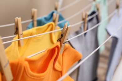 Photo of Different cute baby onesies hanging on clothes line against beige background, closeup. Laundry day