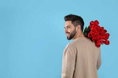Happy man with red tulip bouquet on light blue background, space for text. 8th of March celebration
