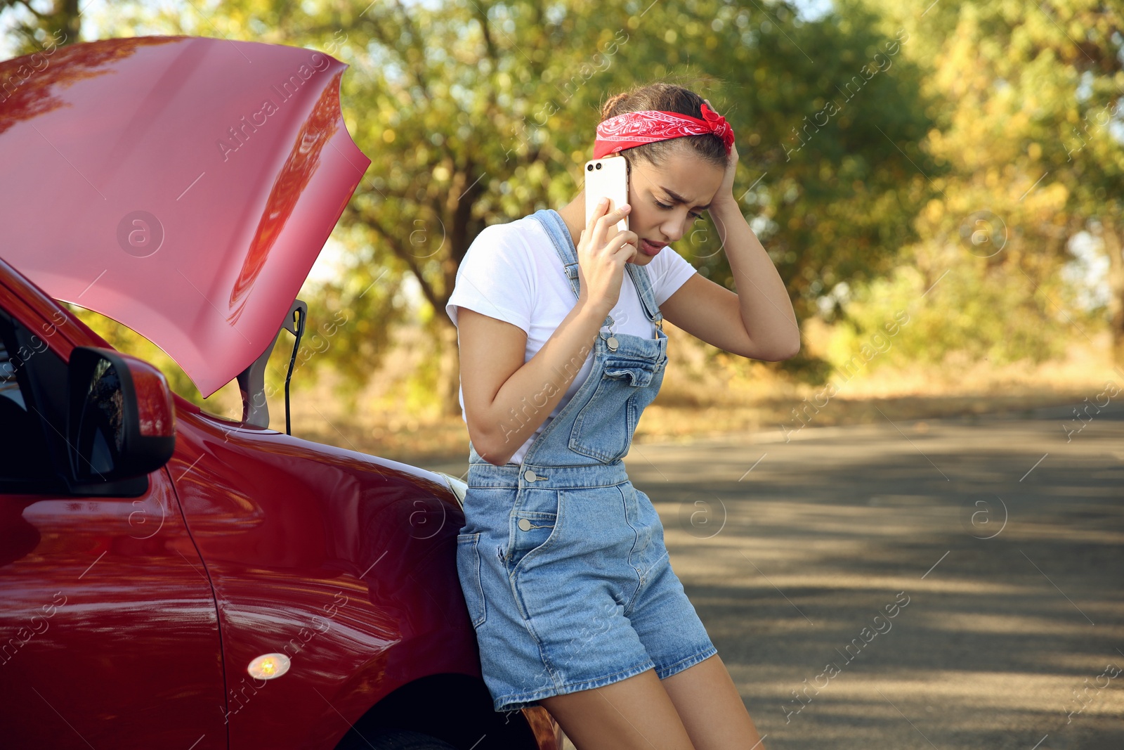 Photo of Stressed woman talking on phone near broken car outdoors