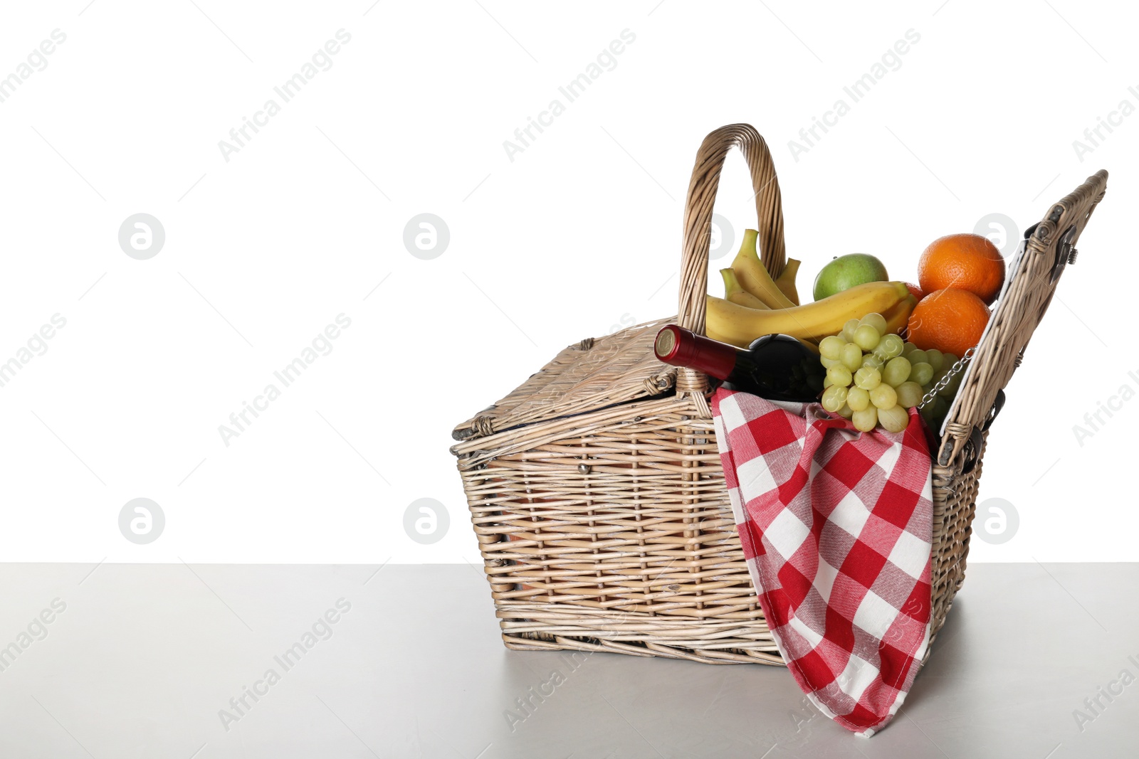 Photo of Wicker picnic basket with wine and different fruits on white background, space for text