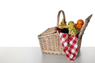 Wicker picnic basket with wine and different fruits on white background, space for text