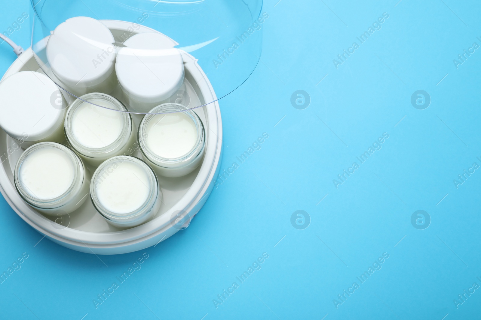 Photo of Modern yogurt maker with full jars on light blue background, top view. Space for text