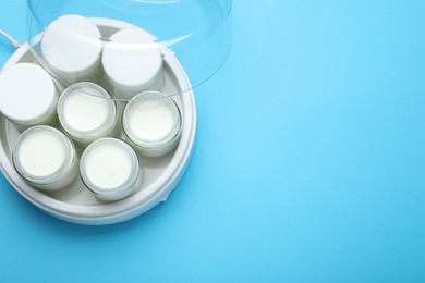 Photo of Modern yogurt maker with full jars on light blue background, top view. Space for text