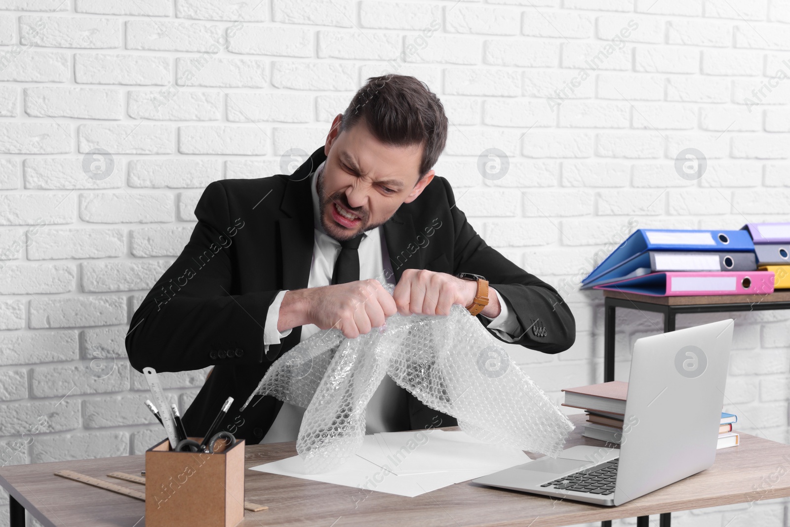 Photo of Businessman popping bubble wrap at workplace in office. Stress relief