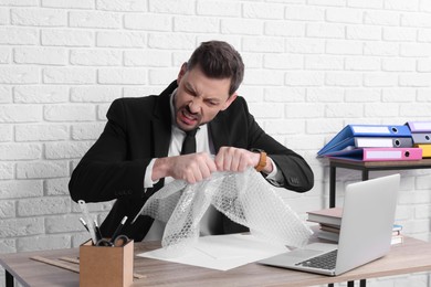 Businessman popping bubble wrap at workplace in office. Stress relief