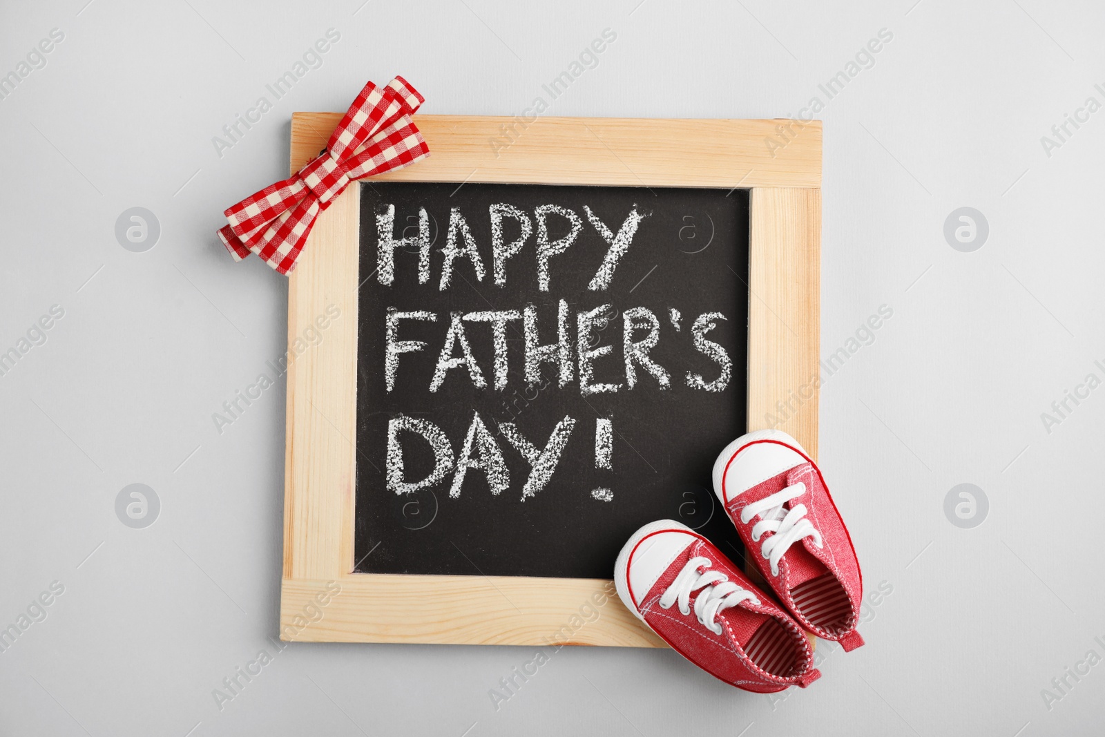 Photo of Flat lay composition with blackboard and baby shoes on gray background. Happy Father's Day