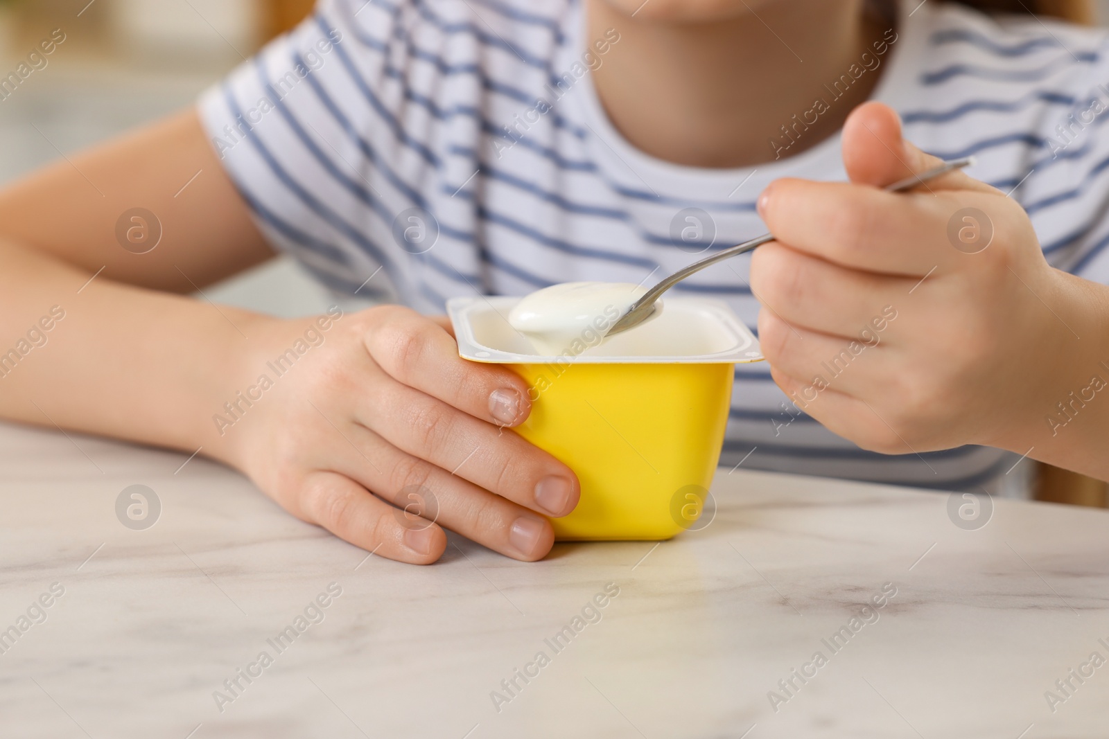 Photo of Cute little girl with tasty yogurt at white marble table, closeup