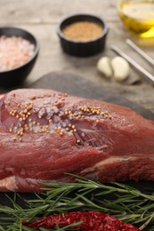 Photo of Piece of raw beef meat, rosemary, spices and chili pepper on table, closeup