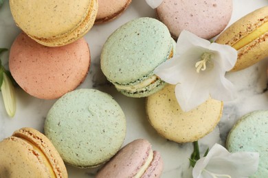 Photo of Delicious macarons and flowers on white marble table, closeup