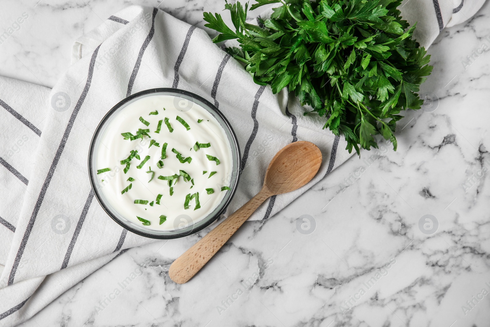 Photo of Glass bowl of fresh sour cream with parsley and wooden spoon on marble table, flat lay. Space for text