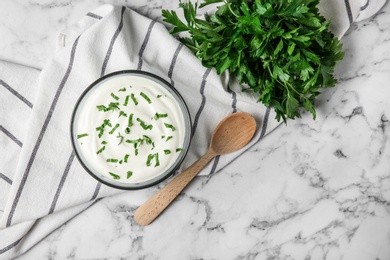 Photo of Glass bowl of fresh sour cream with parsley and wooden spoon on marble table, flat lay. Space for text