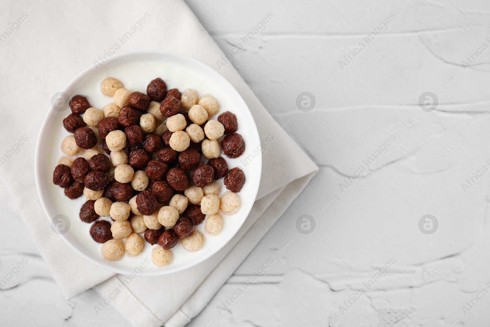 Photo of Breakfast cereal. Tasty corn balls with milk in bowl on white textured table, top view. Space for text