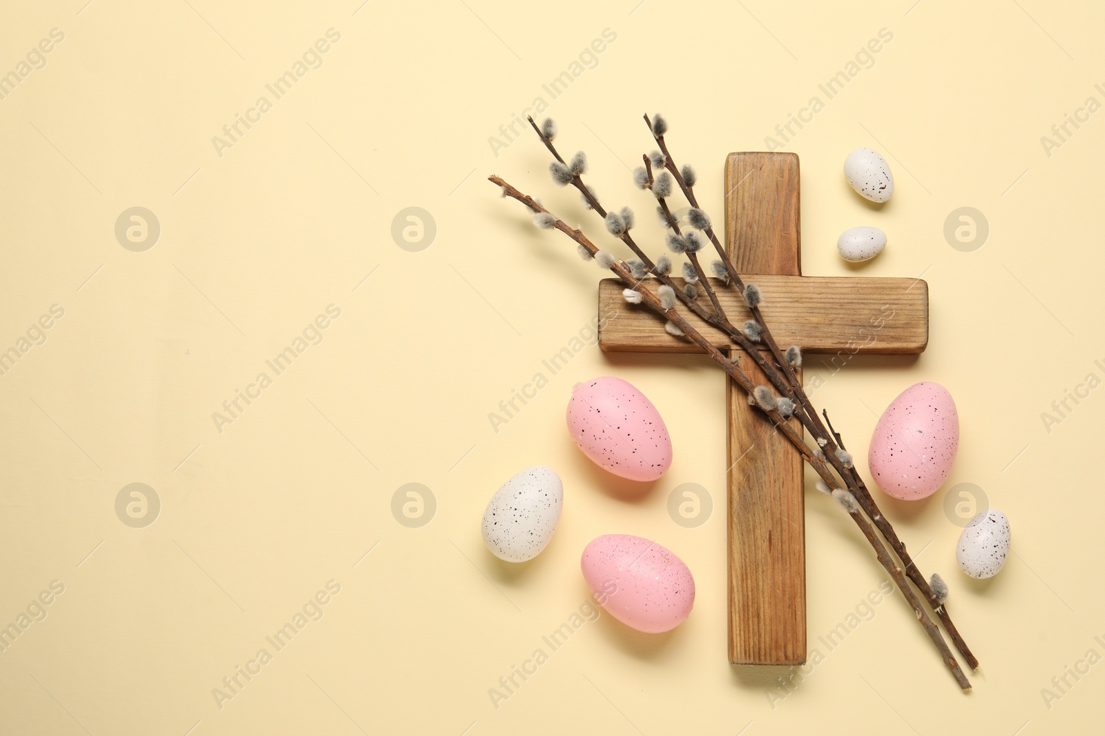 Photo of Wooden cross, painted Easter eggs and willow branches on beige background, flat lay