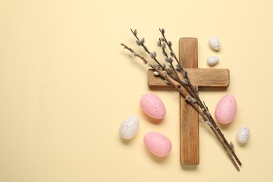 Wooden cross, painted Easter eggs and willow branches on beige background, flat lay