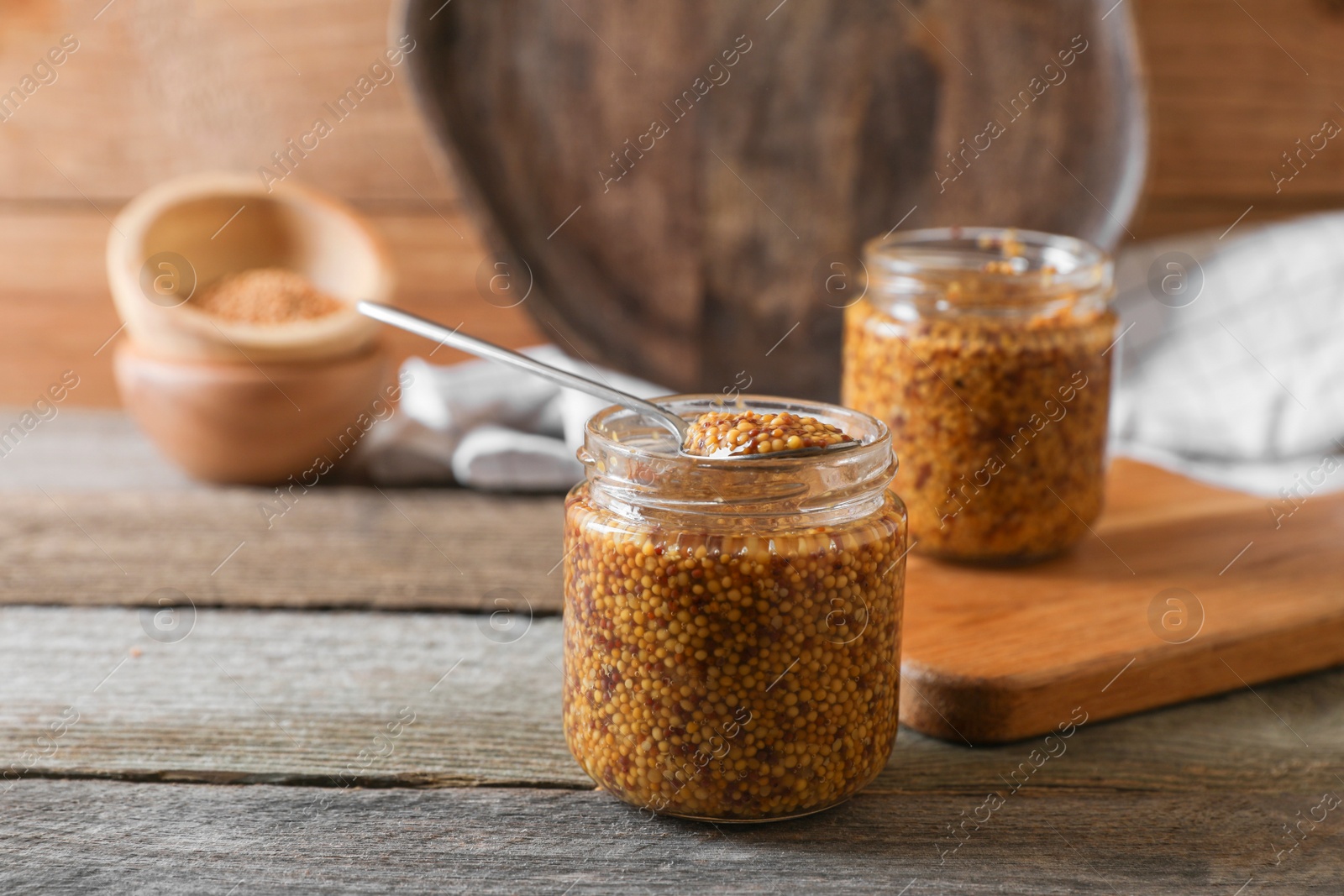 Photo of Jars and spoon of whole grain mustard on wooden table. Space for text