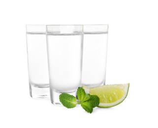 Photo of Shot glasses of vodka with lime and mint on white background
