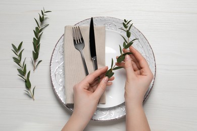 Photo of Woman adjusting stylish table setting with eucalyptus leaves on white wooden background, closeup