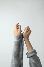 Photo of Woman taking off grey knitted sweater on light background, focus on hands