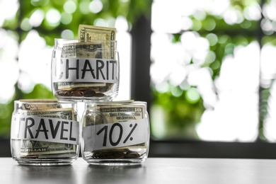 Photo of Glass jars with money for different needs on table against blurred background, space for text