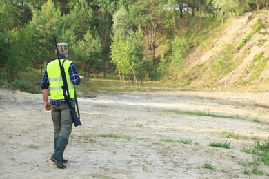 Photo of Man with hunting rifle wearing safety vest outdoors, back view. Space for text
