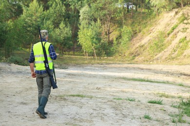 Man with hunting rifle wearing safety vest outdoors, back view. Space for text