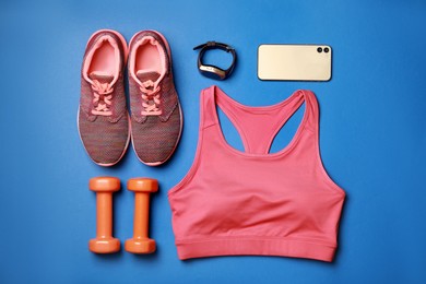 Stylish sportswear, dumbbells and smartphone on blue background, flat lay